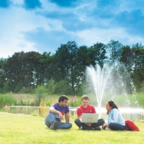 three students sitting on grass looking at laptop